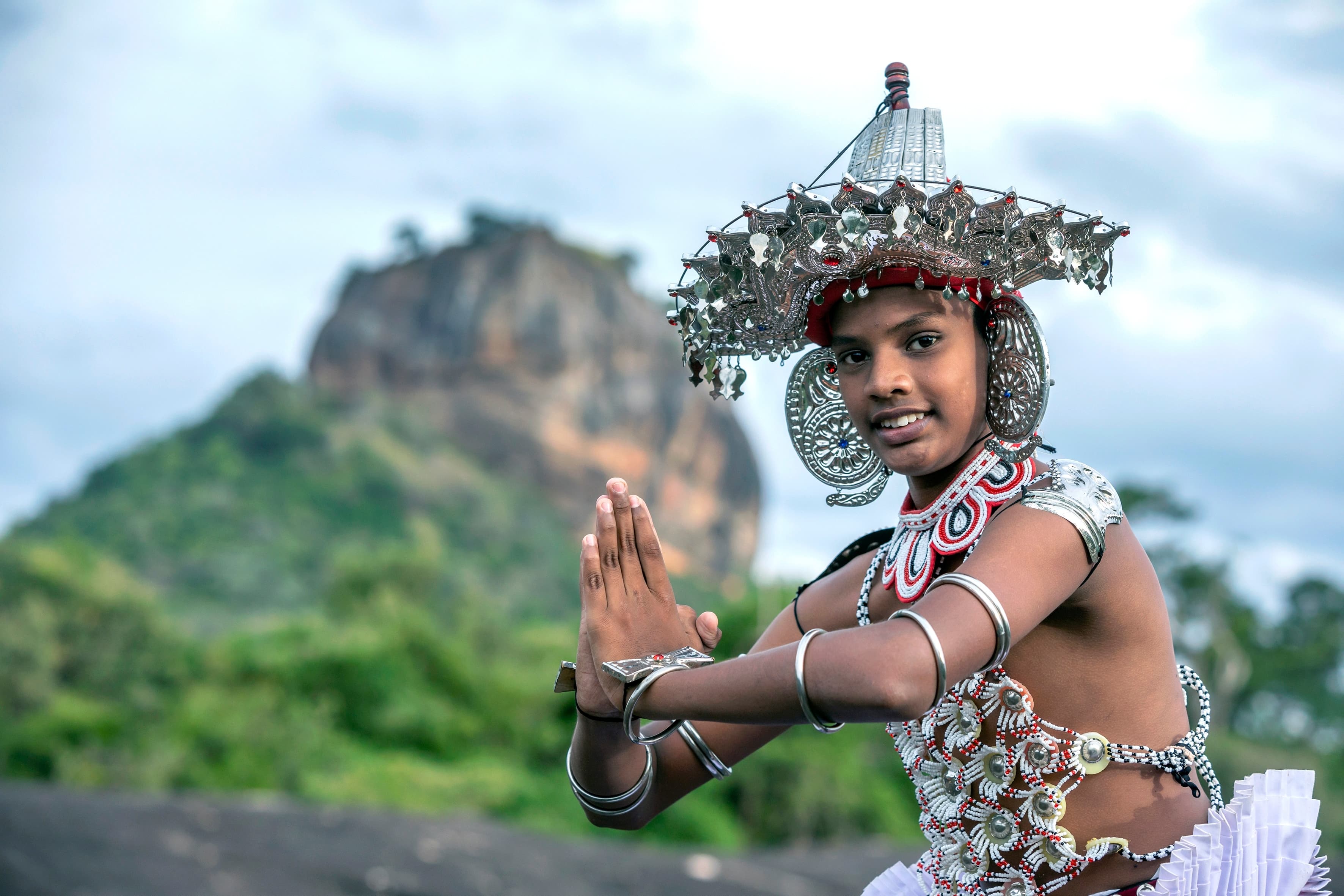 Traditional Kandyan dancer in full costume performing with Sigiriya Lion Rock in the background, representing a cultural triangle tour.