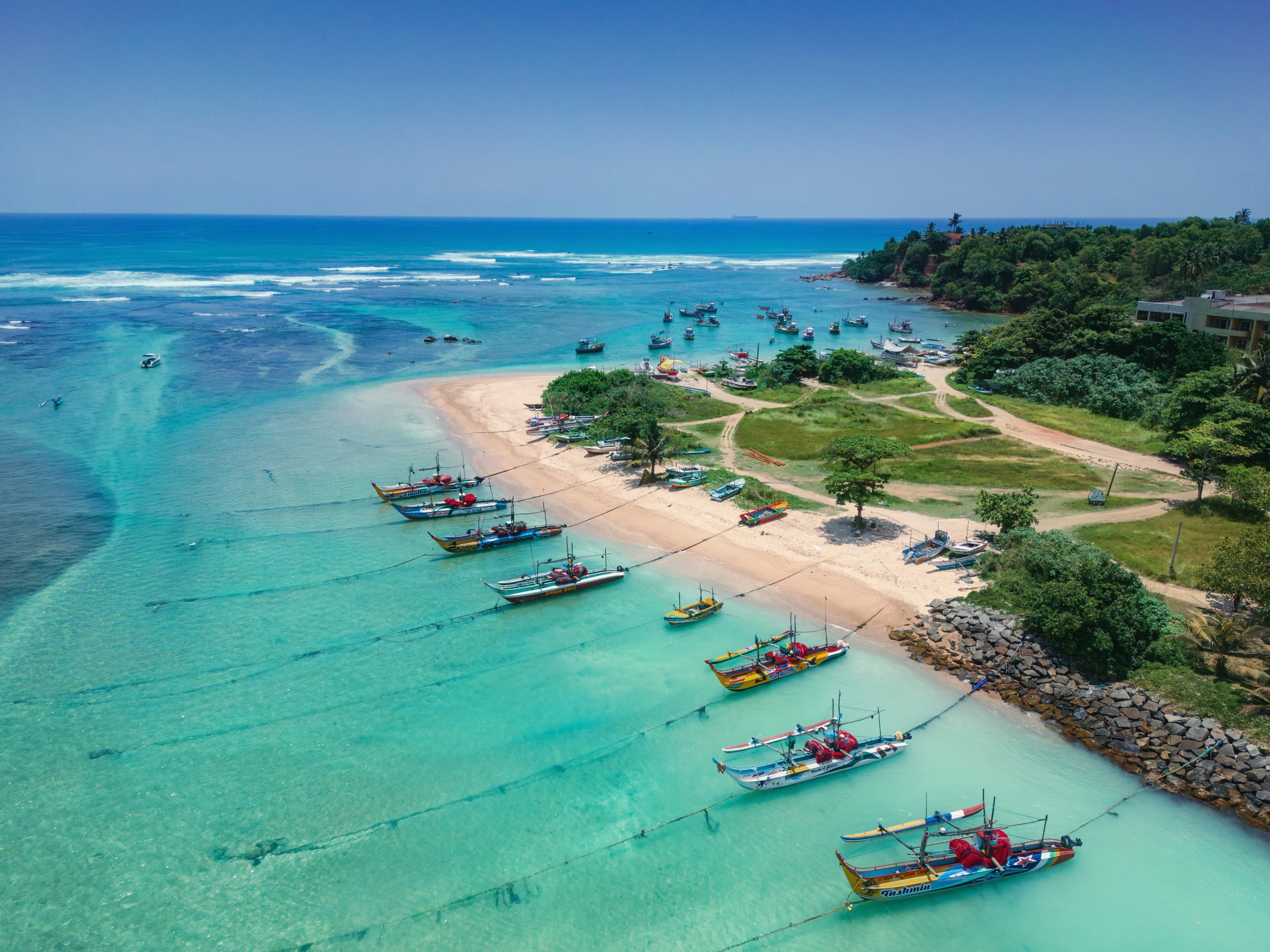 Drone view of colorful fishing boats on the golden sand of a south coast beach in Sri Lanka during a beach holiday tour.