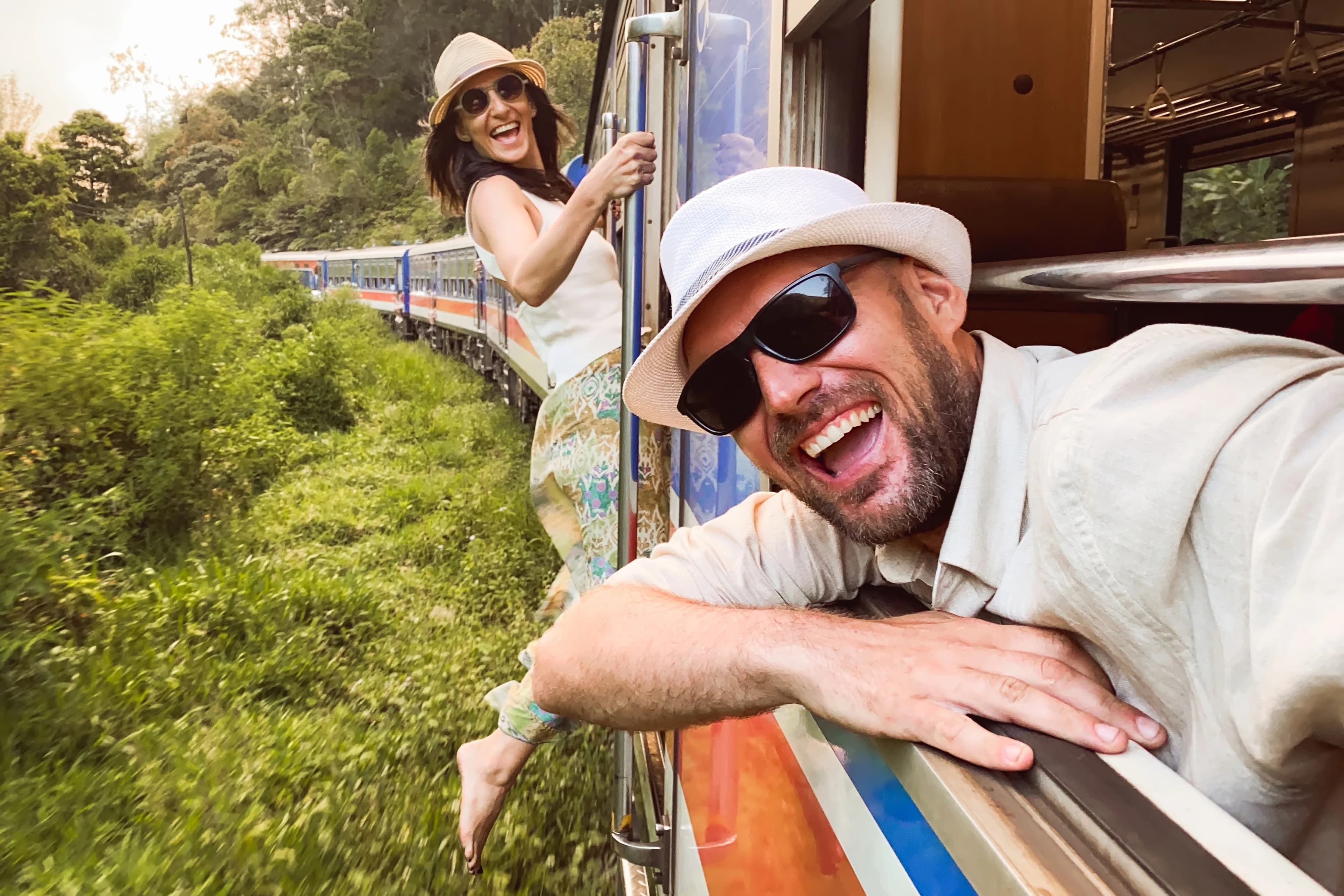 Couple hanging out of the iconic blue train on the scenic Kandy to Ella journey, a must-do Sri Lanka tour.